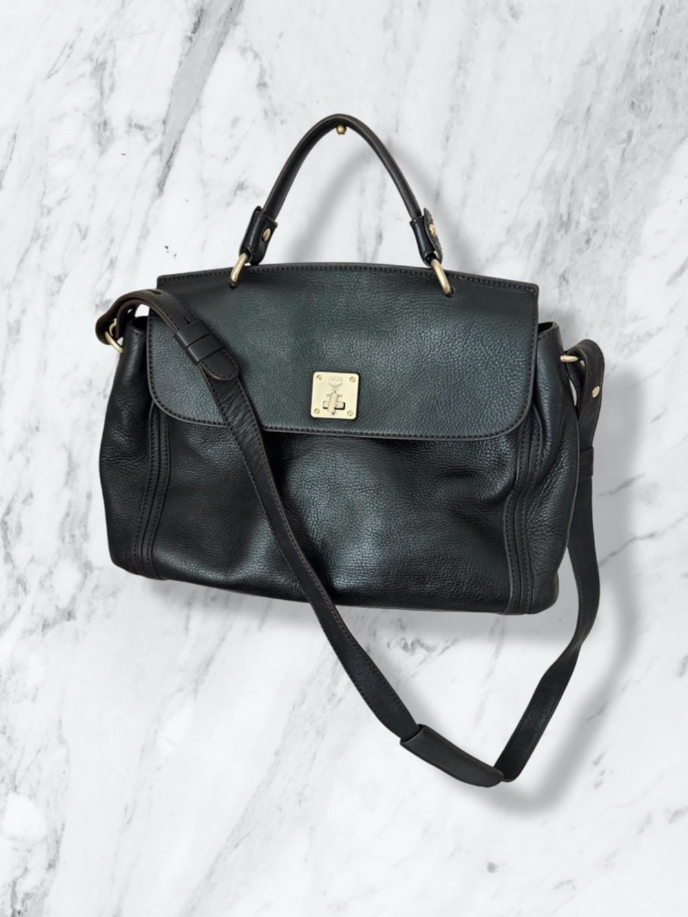 MCM black pebbled leather flap medium top handle bag with a shoulder strap.